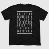 UK Tour product back mockup: original artwork composited onto a realistic black cotton shirt flatlay. Neutral light gray background.